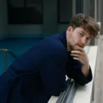 Man in a navy waffle pique spa robe leaning on a railing by the pool