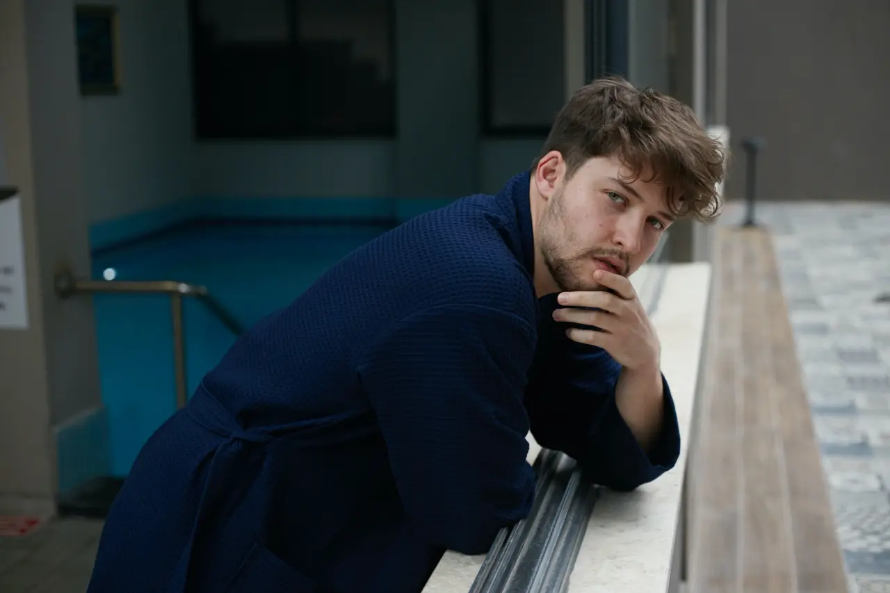 Man in a navy waffle pique spa robe leaning on a railing by the pool