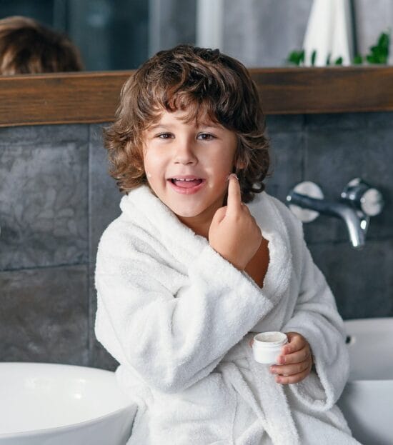 Boy in a white organic cotton kids bathrobe giving a thumbs up in the bathroom