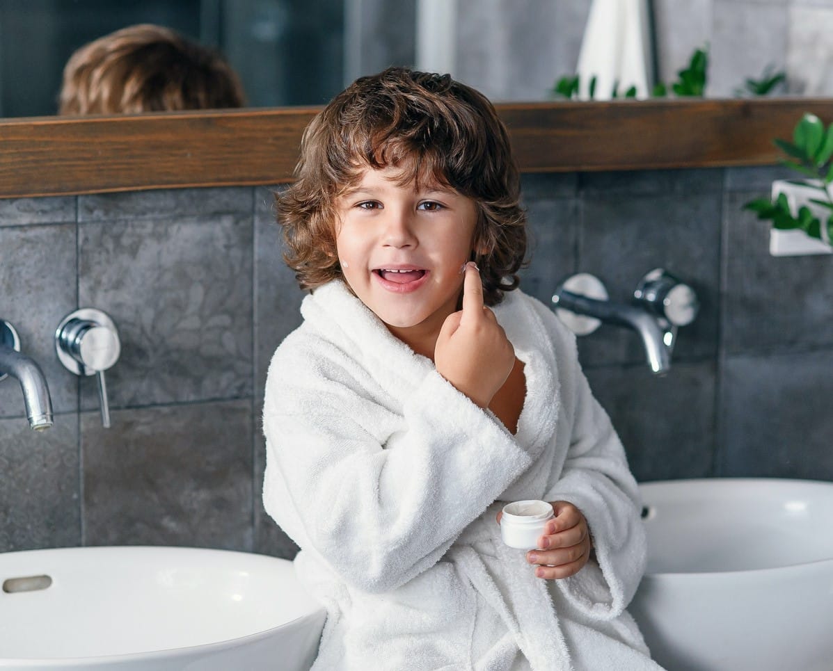 Boy in a white organic cotton kids bathrobe giving a thumbs up in the bathroom
