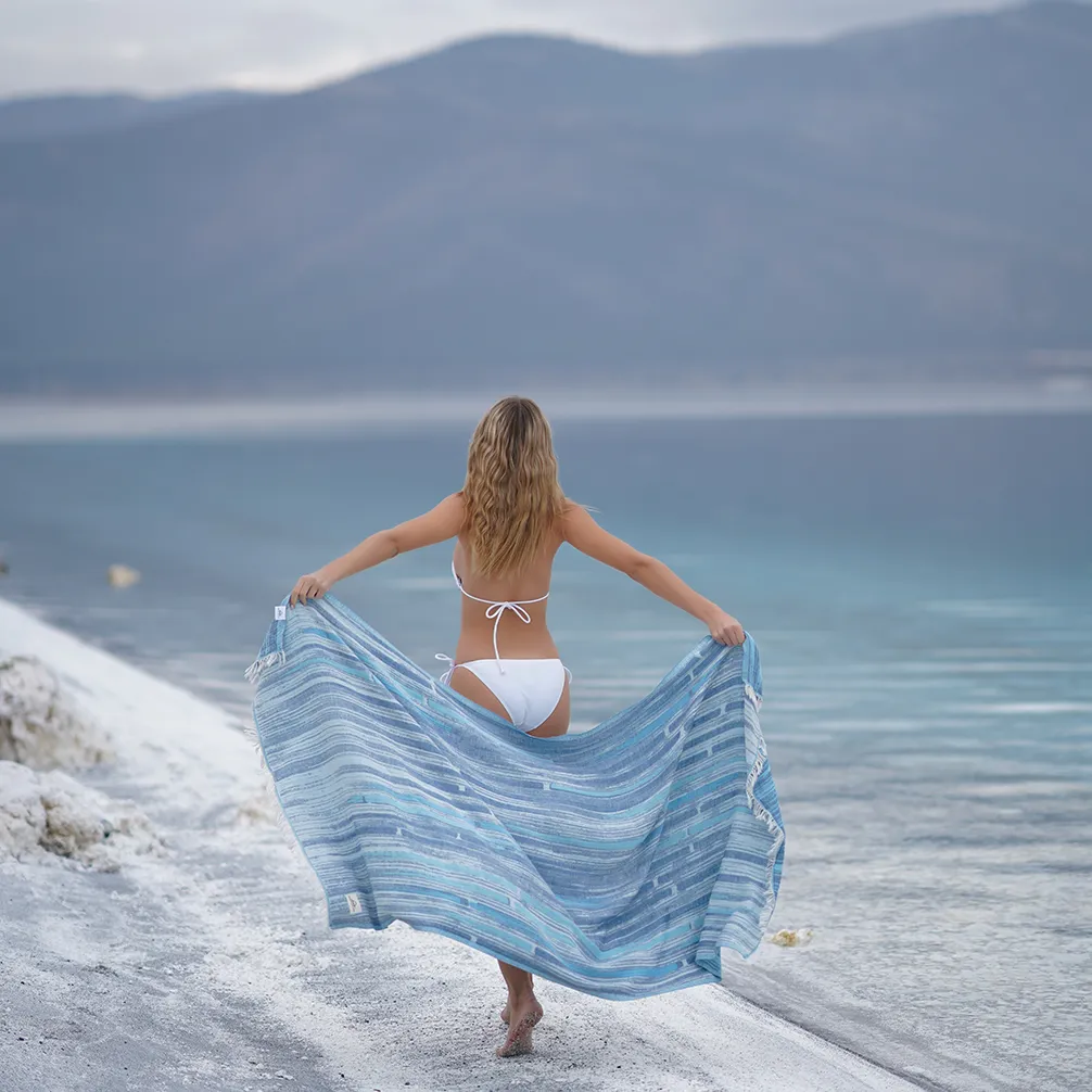 Woman holding the blue Maia Peshtemal Towel open by a lake