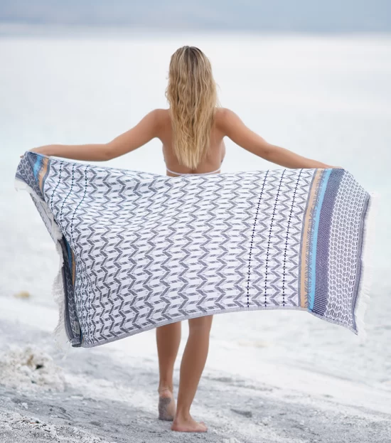 Woman holding the blue Myra Peshtemal Towel open on the beach