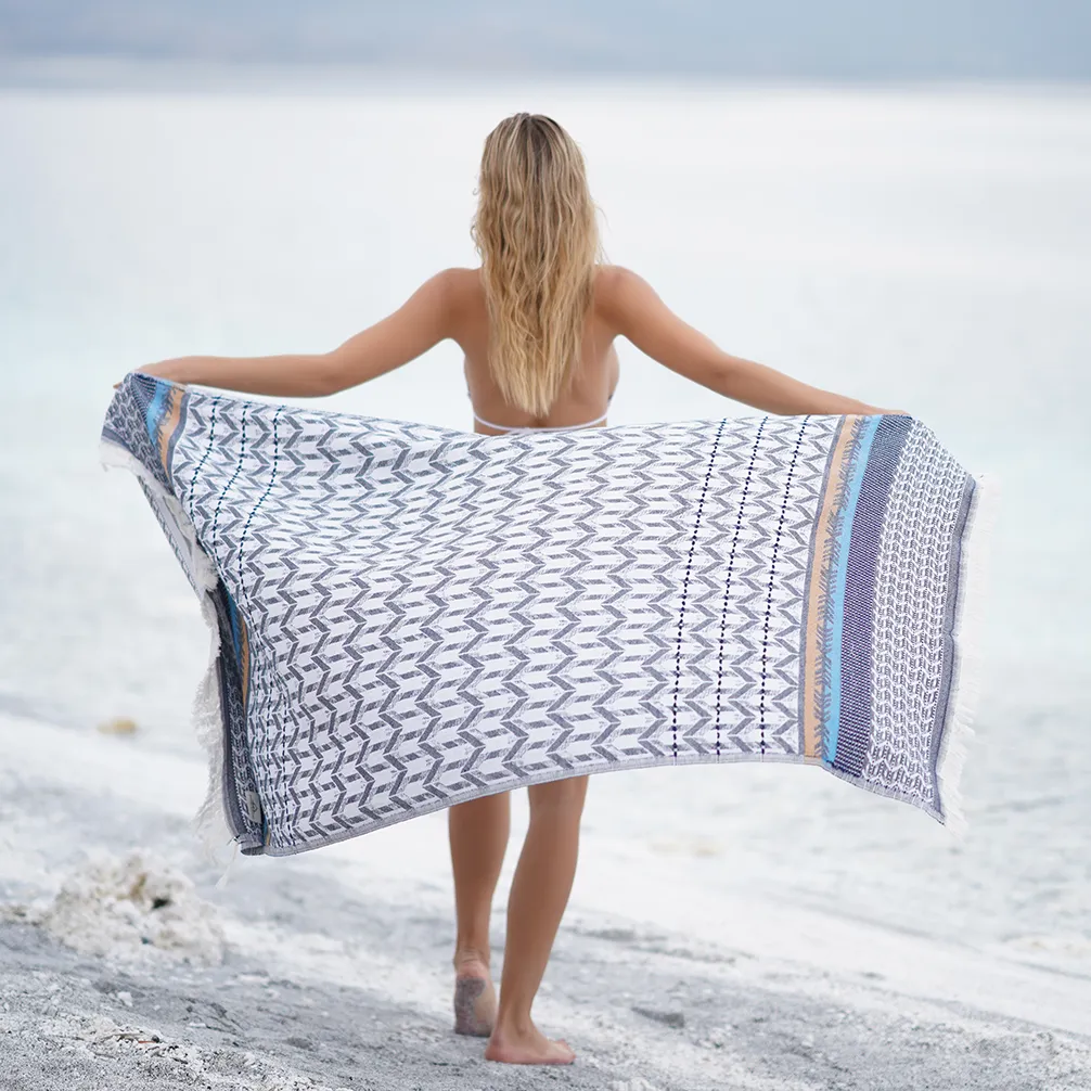 Woman holding the blue Myra Peshtemal Towel open on the beach
