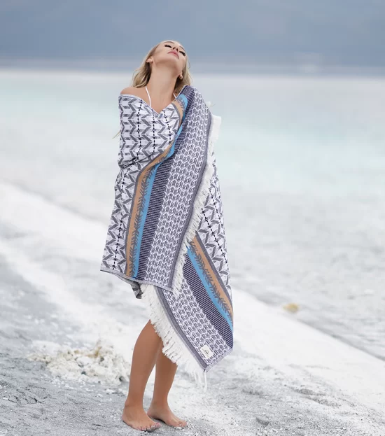Woman wrapped in the blue Myra Peshtemal Towel on the beach