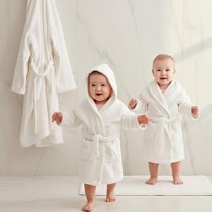 Two toddlers in white Organic Kids Robes, one hooded, standing near hanging towels - Bagno Milano