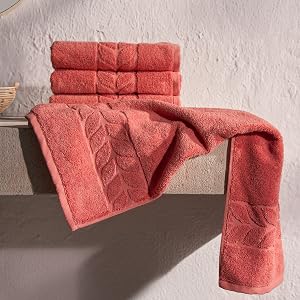 Folded and draped coral jacquard border towels on a stone ledge - Bagno Milano