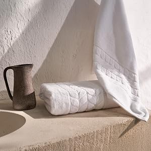 Folded white jacquard border towels with a stone pitcher on a sink ledge - Bagno Milano