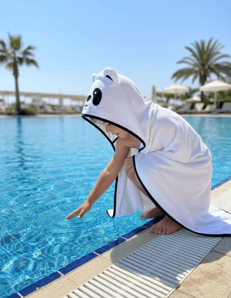 Child in a white panda hooded towel sitting by the pool