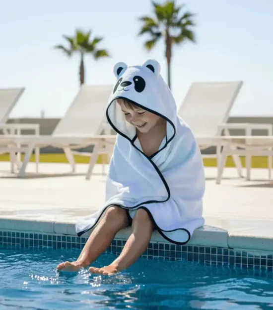 Child in a panda organic cotton hooded towel by the pool